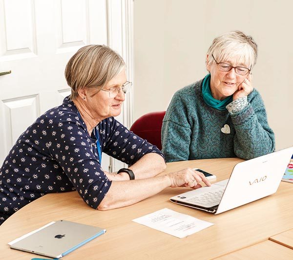 One woman showing another woman how to use a laptop. They are both sitting at a table.